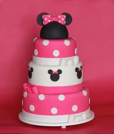 a pink and white cake with minnie mouse on top, sitting in front of a red background