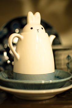 a ceramic teapot with a bunny face on it sitting in front of other plates