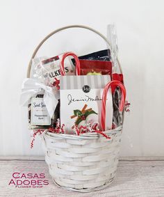 a white basket filled with candy canes, candies and other holiday treats sitting on top of a wooden floor