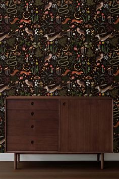 a cabinet with drawers in front of a wallpapered background that has animals and plants on it