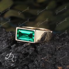 a ring with an emerald colored stone in the center on top of a black rock