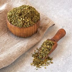 a wooden bowl filled with dried herbs next to a spoon on top of a cloth