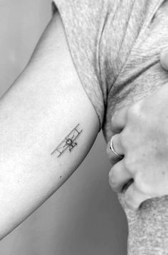 a small airplane tattoo on the left inner arm and shoulder, with an arrow in the middle