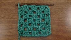 a green crochet square sitting on top of a wooden table next to a knitting needle