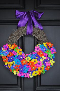 a wreath made out of buttons is hanging on a door with purple ribbon and bow