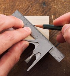 two hands are working on a piece of wood with a ruler and pencils in front of them