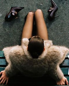 a woman sitting on top of a wooden bench next to high heel shoes and papers