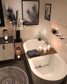 a white bath tub sitting in a bathroom next to two candles and pictures on the wall