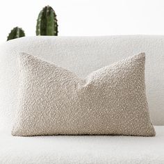 a close up of a pillow on a couch with a cacti in the background