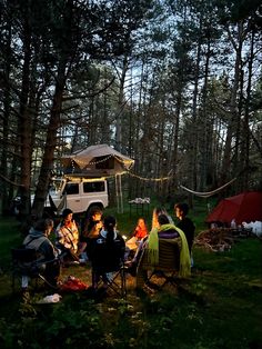 a group of people sitting around a campfire in the middle of a wooded area