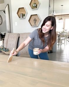 a woman holding a coffee cup while standing next to a wooden table