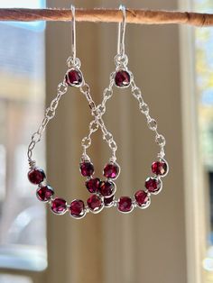 a pair of red glass beads hanging from a hook on a wooden stick in front of a window