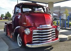 an old red truck parked in front of a gas station