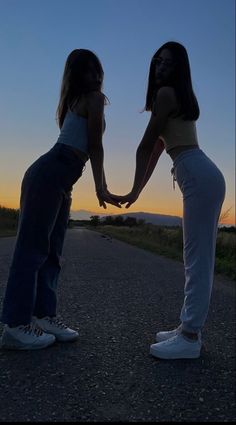 two girls holding hands while standing on the side of a road at sunset or dawn