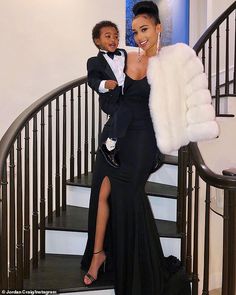 a woman in a black dress standing next to a child on a stair case holding a fur coat