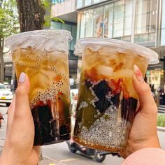 two people holding up drinks in their hands on the side of the road with cars behind them