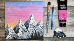 painting supplies including paint, brushes and acrylic paints on a wooden surface with mountains in the background