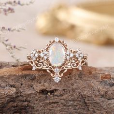 a white opal and diamond ring sitting on top of a piece of drift wood