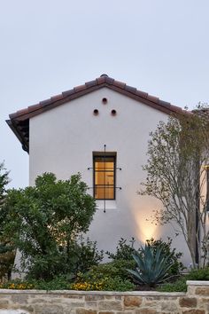 a white house with an orange light on it's window and some plants in front