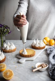 a woman is decorating small pies with whipped cream on top and orange slices around the edges