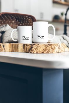 two white coffee mugs sitting on top of a wooden cutting board next to a kitchen counter