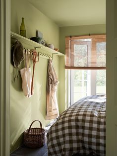 a bed sitting under a window next to a wooden shelf filled with bags and purses