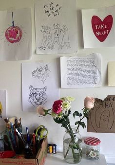 several drawings are hanging on the wall above a vase filled with flowers and pencils