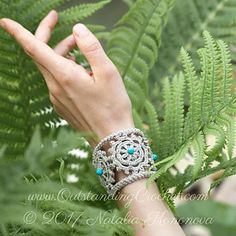 a woman's hand with bracelets on her wrist and fern leaves in the background