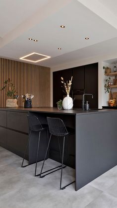 a modern kitchen with two bar stools next to the counter and an island in front of it