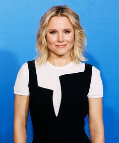 a woman with blonde hair wearing a black and white dress smiles at the camera while standing in front of a blue background