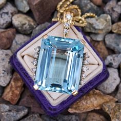 This stunning pendant necklace is centered with an emerald cut aquamarine, weighing 46.22 carats, in a four-prong basket setting. The aquamarine is accented with a total of ten (10) three-prong set round brilliant cut diamonds. The pendant is topped by a enhancer bail three-prong set with three (3) round brilliant cut diamonds. The pendant measures 41.6mm long, including the bail, by 26.0mm wide and 14.8mm deep on an 18.5 inch long, 1.7mm fancy link chain, finished with a lobster clasp. White Gold Aquamarine Pendant Jewelry, Gold Aquamarine Pendant Necklace, Yellow Gold Aquamarine Pendant Jewelry, Aquamarine Stone Ring, Aquamarine Pendant With Natural Stones, Blue Aquamarine Pendant Necklace, Aquamarine Ring Vintage, Aquamarine Pendant, Aquamarine Necklace