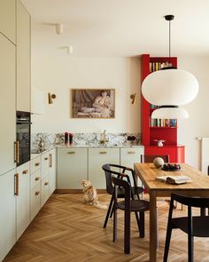 a cat sitting on the floor in a kitchen next to a table with chairs and a bookshelf