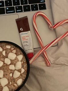 a cup of hot chocolate with marshmallows next to a laptop and candy cane