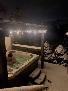 a hot tub in the middle of a snowy yard with christmas lights strung around it