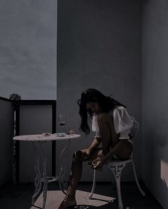 a woman sitting on a chair next to a table with a glass of wine in it