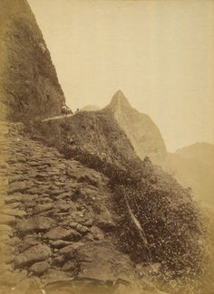 an old black and white photo of some rocks on the side of a mountain with mountains in the background