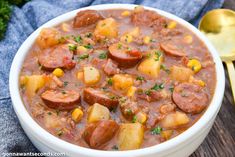 a white bowl filled with stew and potatoes on top of a wooden table next to a spoon