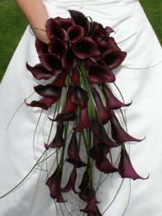 a woman in a wedding dress holding a bouquet of red calla lilies and greenery