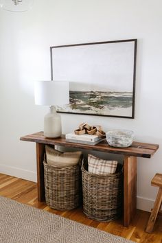 a wooden table with baskets underneath it and a painting on the wall