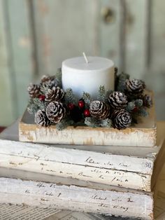 a white candle sitting on top of a wooden box filled with pine cones and berries