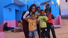 a woman posing for a photo with children in front of a blue building on the beach