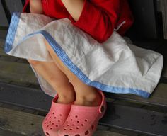 a young child sitting on top of a bed wearing pink shoes and a red shirt