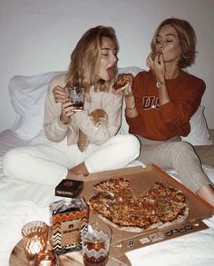 two women sitting on a bed eating pizza