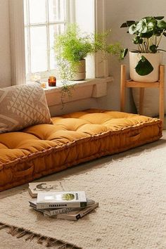 an orange futon sofa in front of a window with potted plants on it