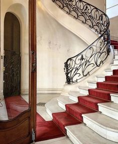 a red carpeted stair case next to a wooden door and white stairs with wrought iron railings