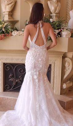 a woman in a white wedding dress standing next to a fireplace with flowers on it