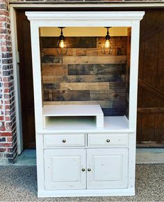 a white cabinet with two lights on the top and one light on the bottom, in front of a brick wall