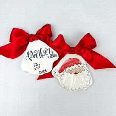 two ceramic ornaments with red ribbon on white fabric, one has a santa clause ornament