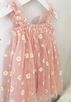 a pink dress with daisies on it hanging from a white hanger next to a wall