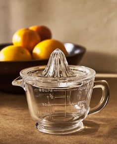 a glass measuring cup sitting on top of a counter next to oranges and a bowl